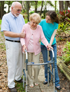 An elderly man and his granddaughter are helping an elderly woman with a walker. 