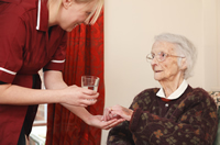 Una enfermera le da medicamento y un vaso de agua a una mujer mayor  
