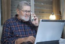 Un hombre  sentado frente a una computadora busca información sobre la salud mientras  habla por  teléfono